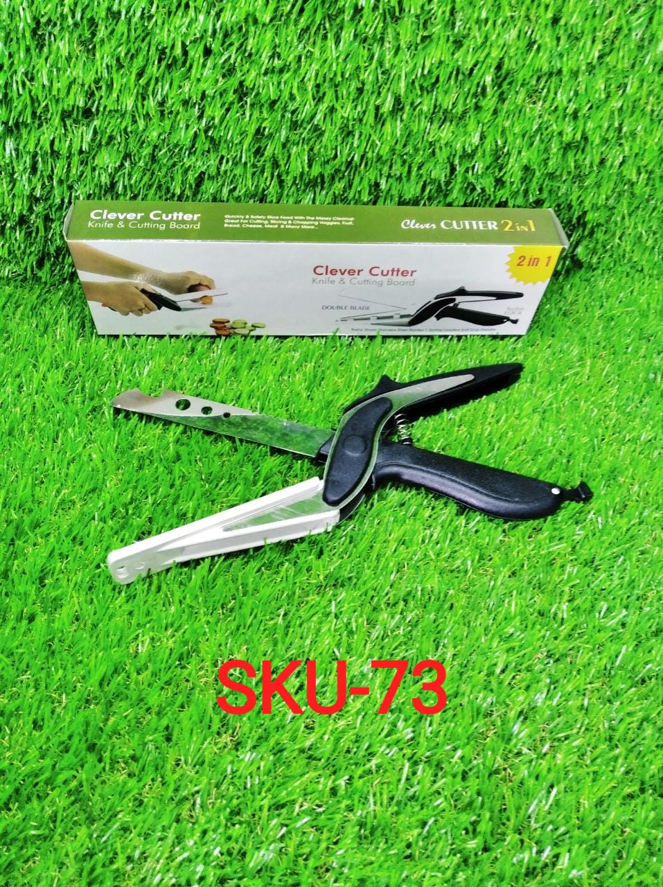 A black and white clever cutter and its product box are displayed on a vibrant green artificial grass background.