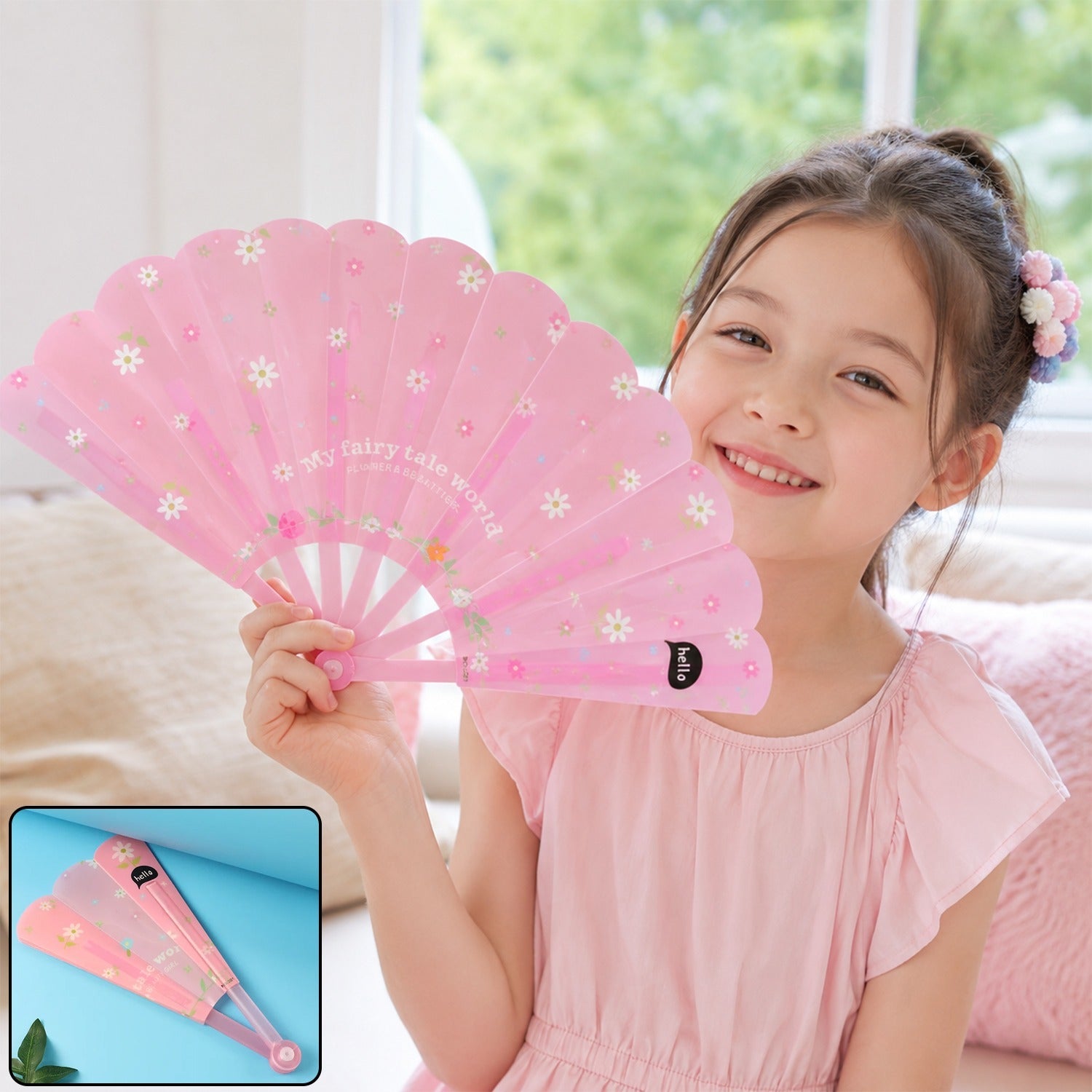 A young girl in a pink dress smiles while holding an open pink folding fan decorated with white flowers and text.