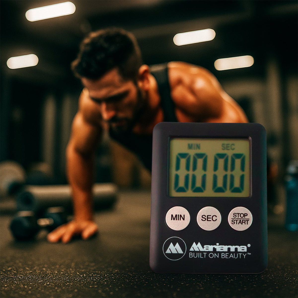A black digital timer displaying 00:00 in the foreground, with a man doing push-ups in a gym in the background.