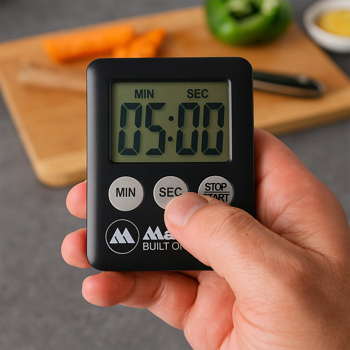 A hand adjusts the 'SEC' button on a black digital timer displaying 05:00, with a cutting board in the background.