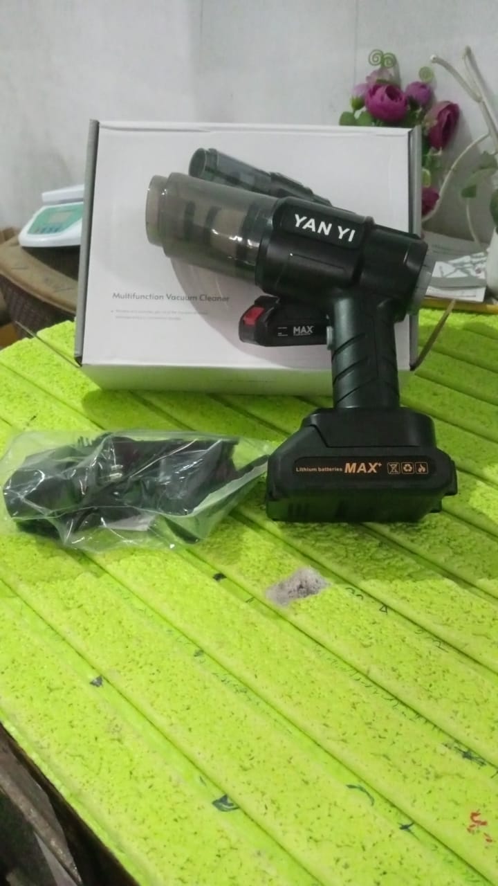 Black handheld vacuum cleaner with a clear dustbin and battery pack, next to its white box and a plastic-wrapped accessory
