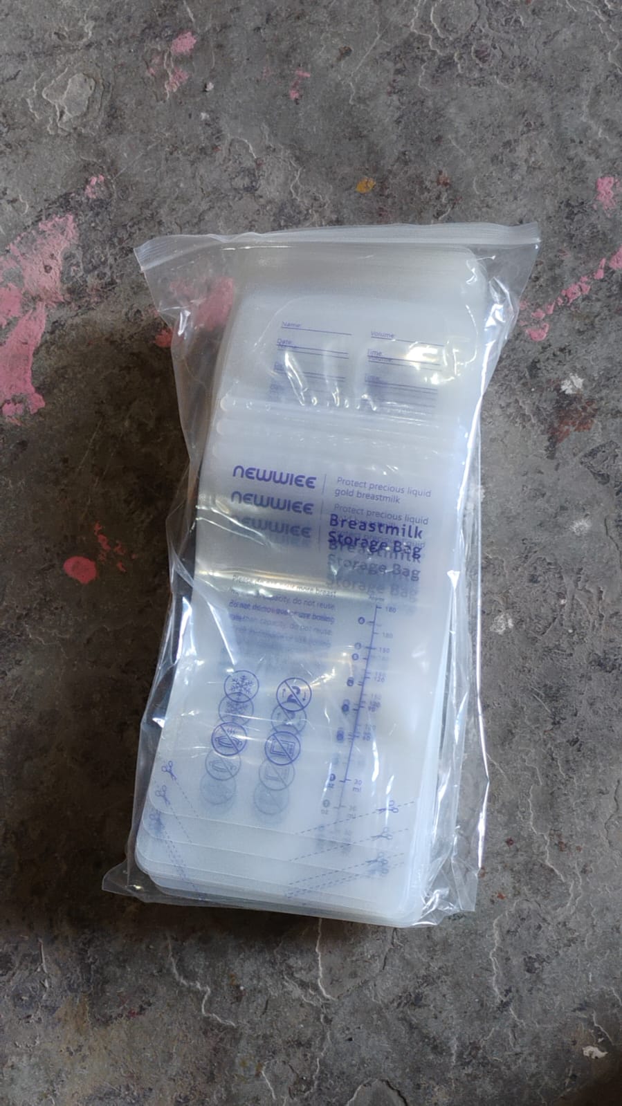 A stack of clear breastmilk storage bags with blue text and markings, packaged in a plastic bag on a grey surface.