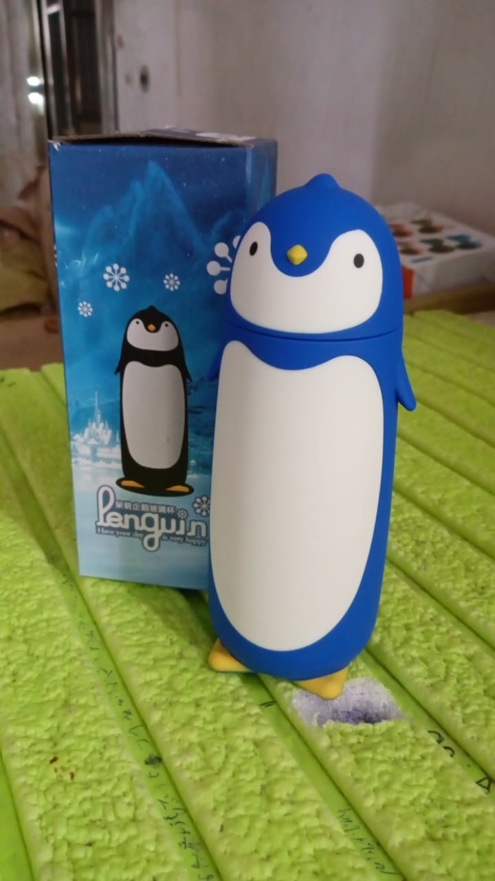 Blue penguin water bottle with its matching illustrated box, sitting on a green textured surface.
