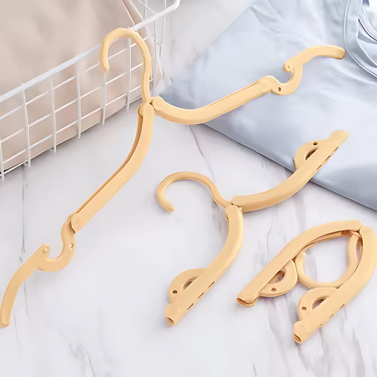 Three beige foldable clothes hangers, one extended, one partially folded, and one fully folded, are on a marble surface.
