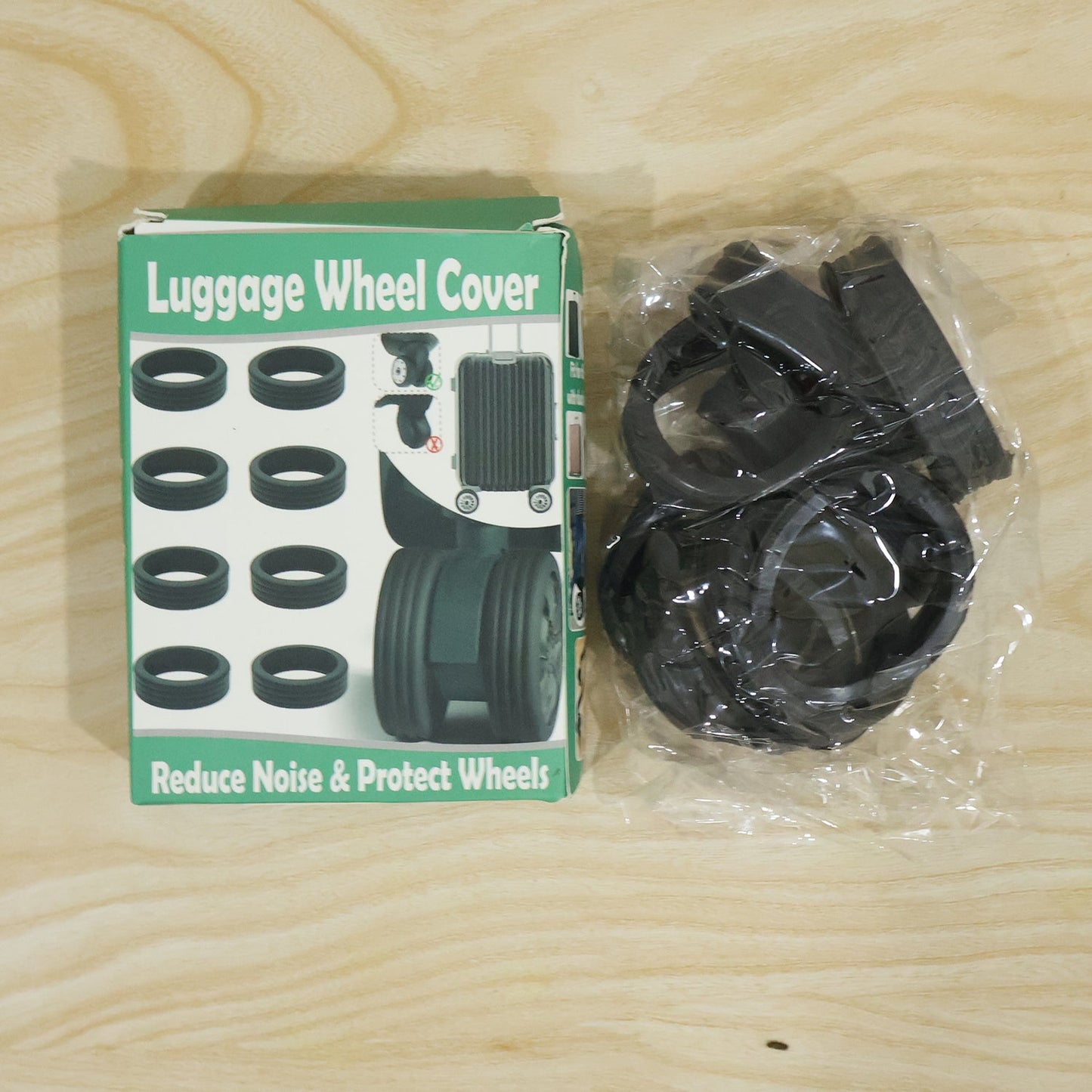 A green and white box labeled "Luggage Wheel Cover" next to a clear plastic bag filled with black silicone rings on a wooden