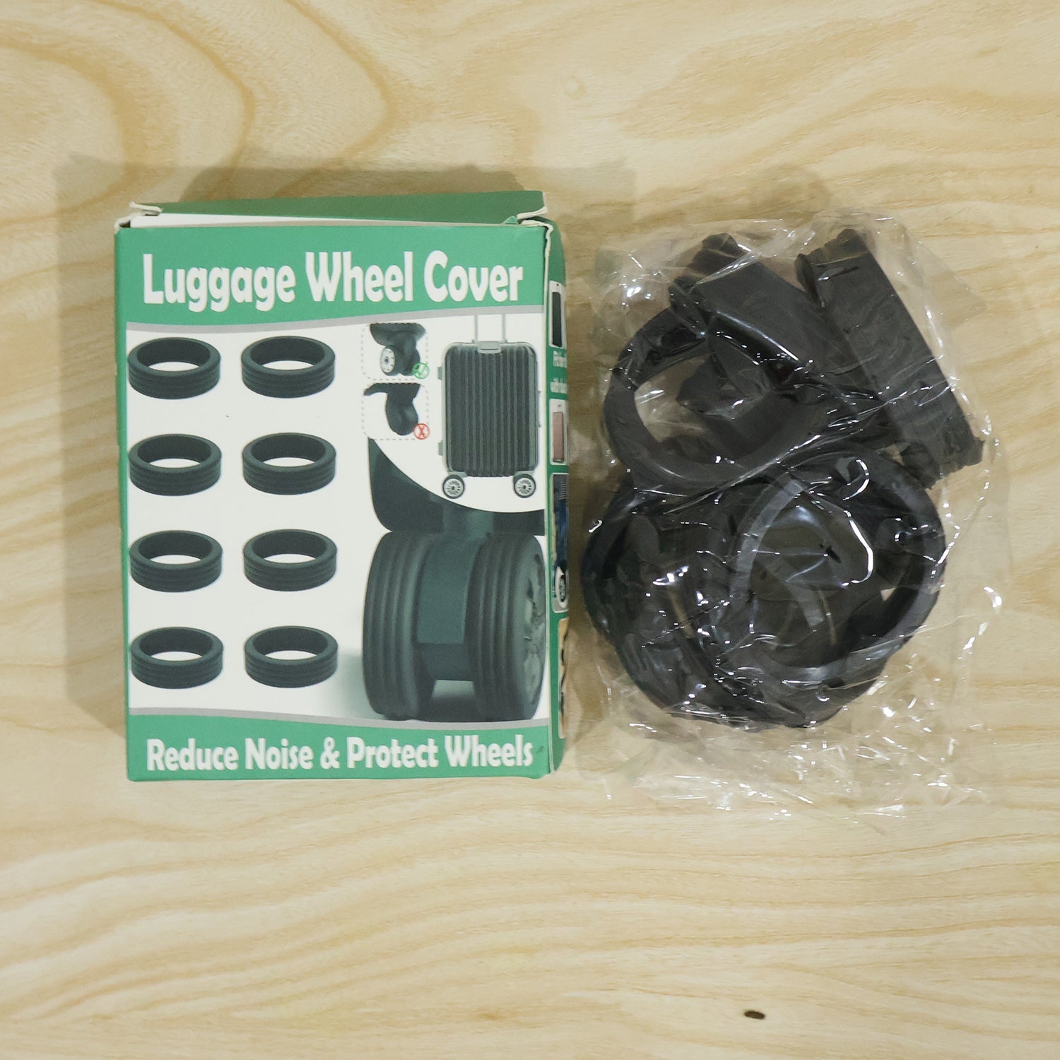 A green and white box labeled "Luggage Wheel Cover" next to a clear plastic bag filled with black silicone rings on a wooden