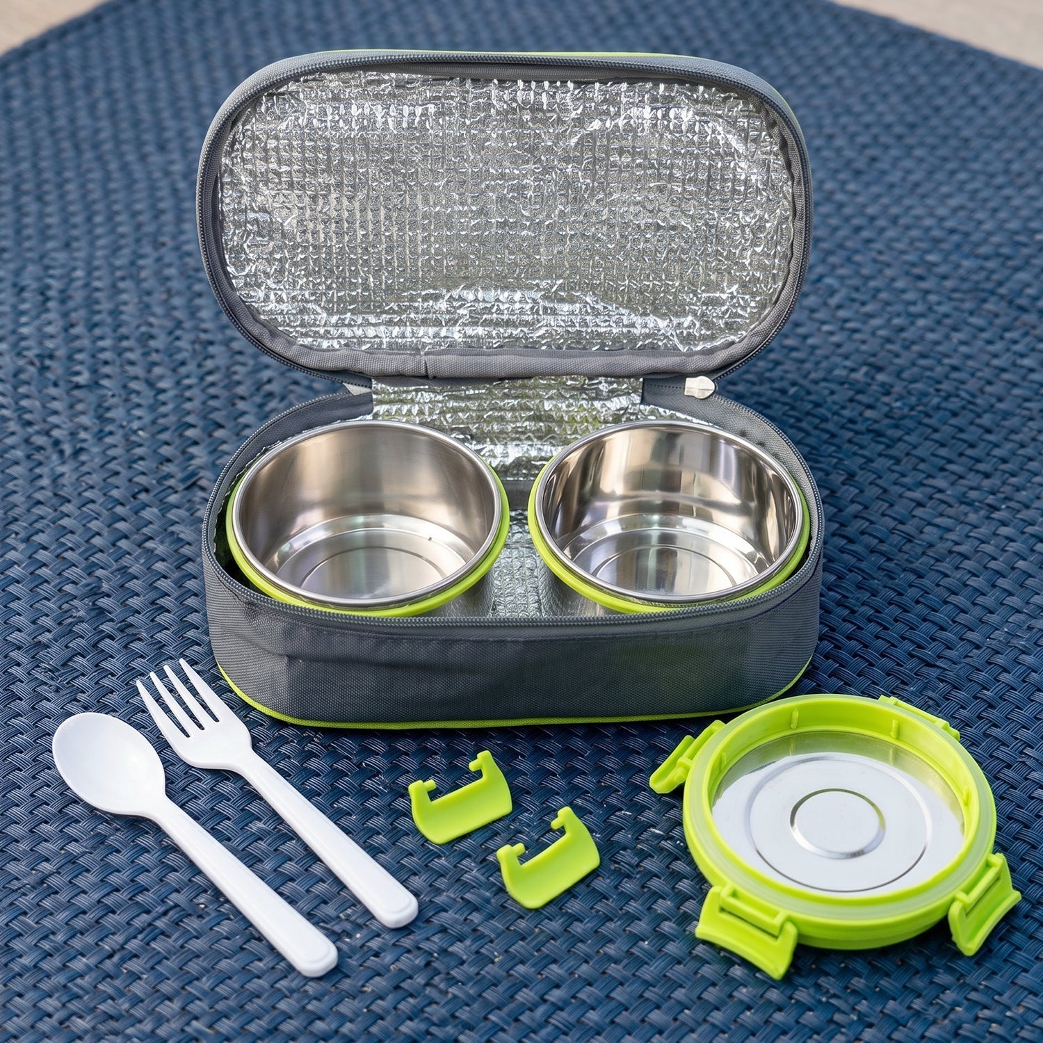 An open grey and lime green insulated lunch bag with two empty stainless steel containers, cutlery, and lid on a blue