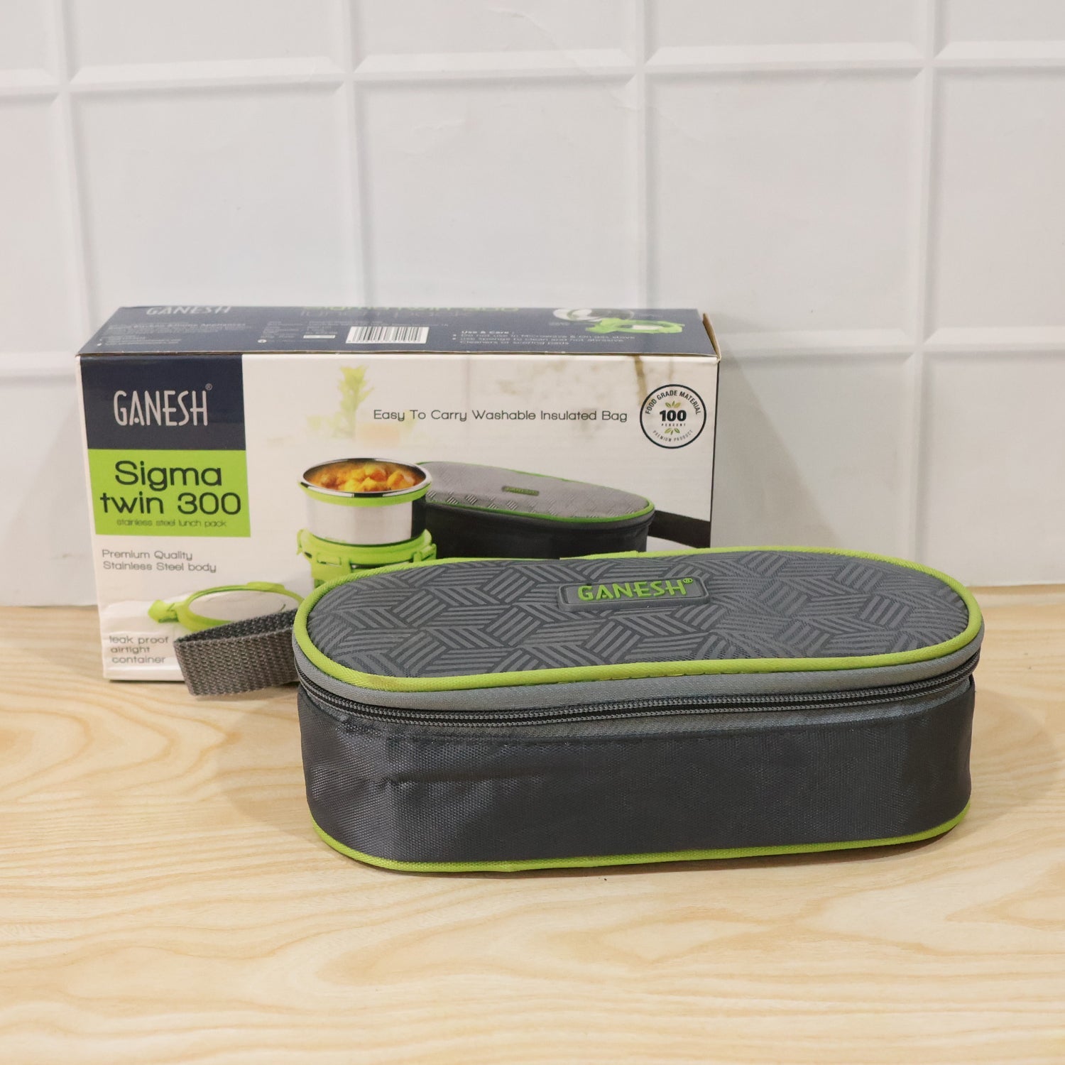 A closed grey and lime green insulated lunch bag with a geometric pattern next to its product box on a wooden surface.