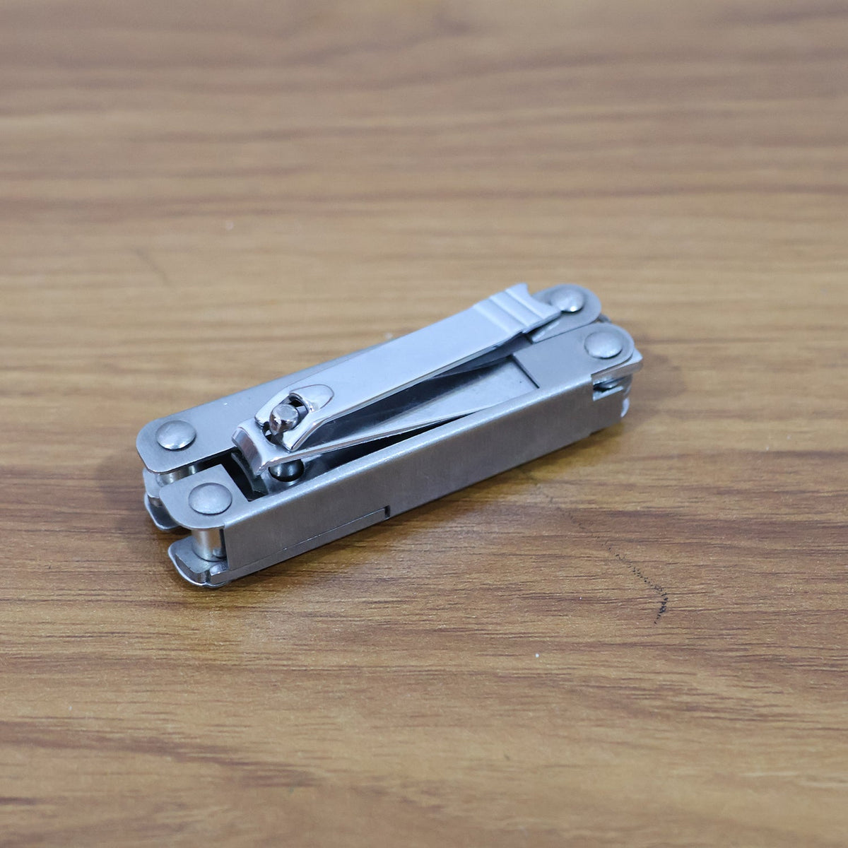 A folded silver multi-tool with a keyring rests on a warm-toned wooden surface.