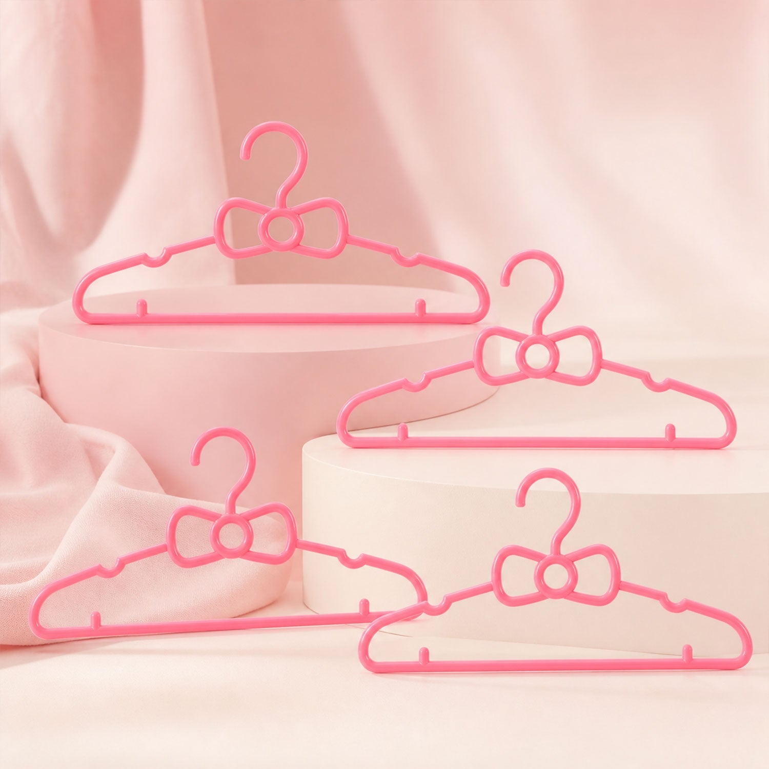 Four pink plastic bow-shaped hangers are arranged on and around two pink display blocks on a pink background.