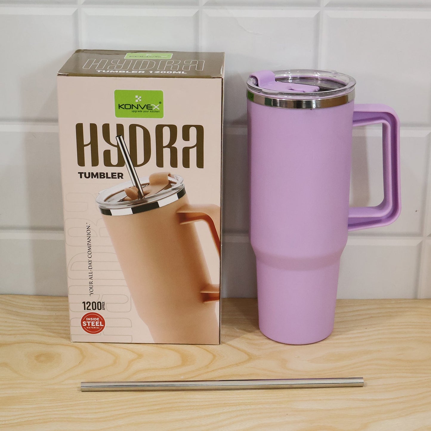 A purple Konvex Hydra Insulated Travel Tumbler, its box, and a metal straw are arranged on a wooden surface with a white