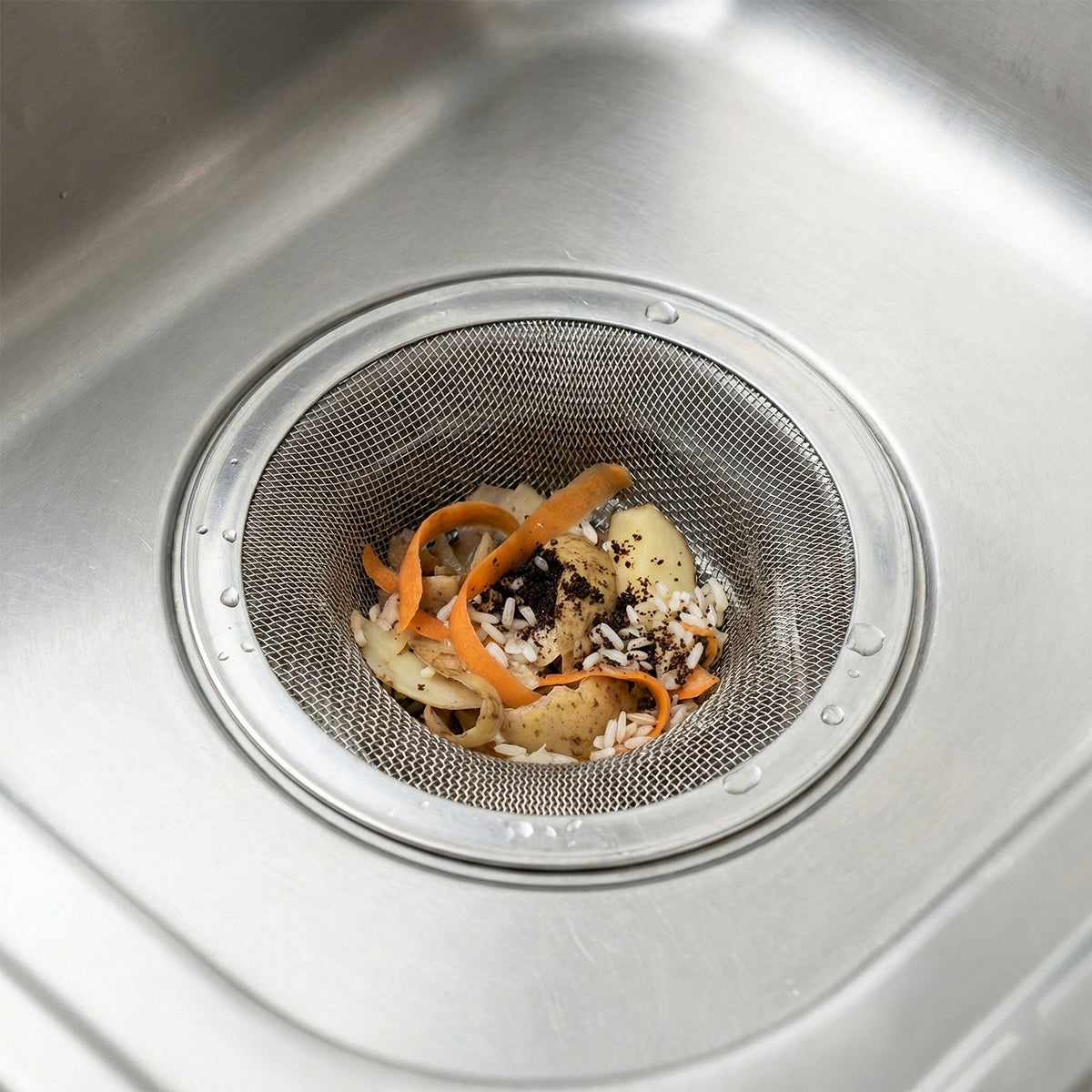 A close-up of a stainless steel mesh sink strainer filled with food scraps in a sink.