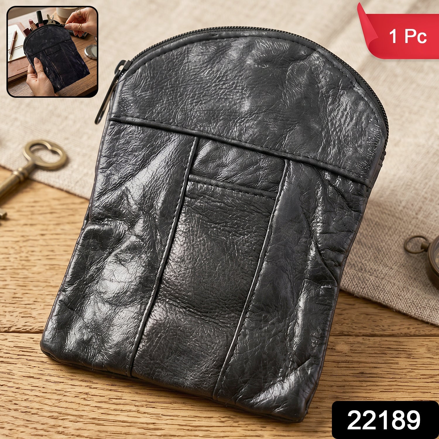 A black leather pouch with a zipper closure resting on a wooden surface with a key and compass.