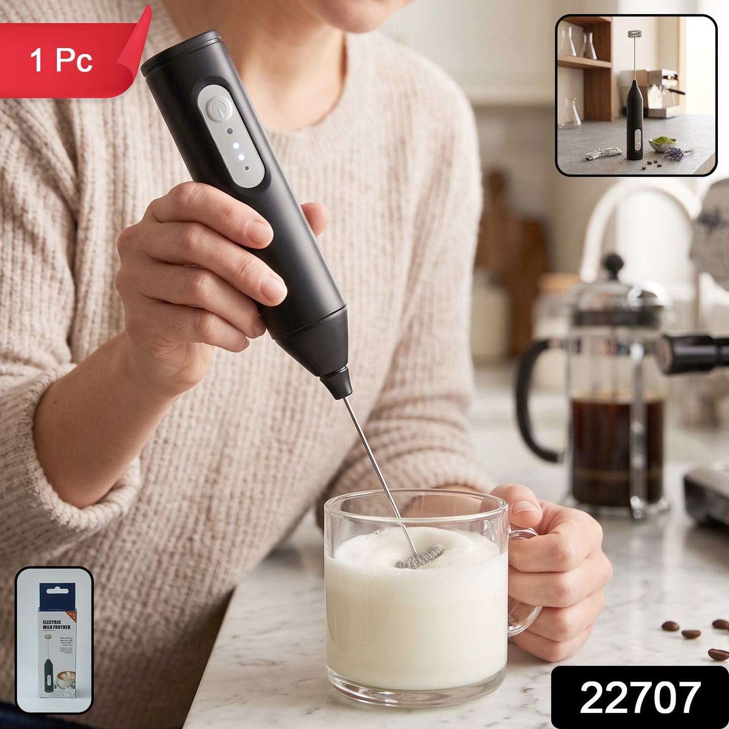 A person in a beige sweater uses a black electric milk frother to whisk milk in a clear glass mug on a marble counter.