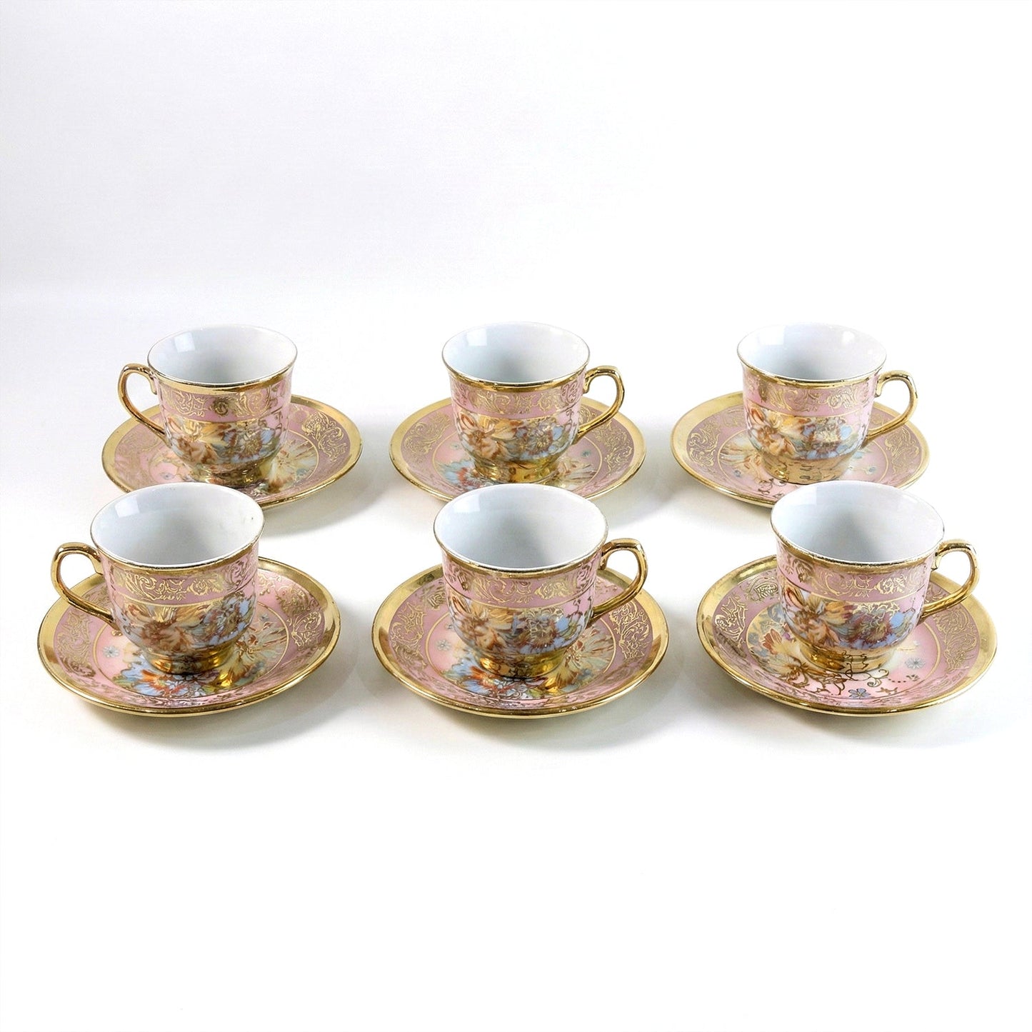Six pink and gold floral porcelain teacups and saucers with gold rims and handles are neatly arranged on a white surface.
