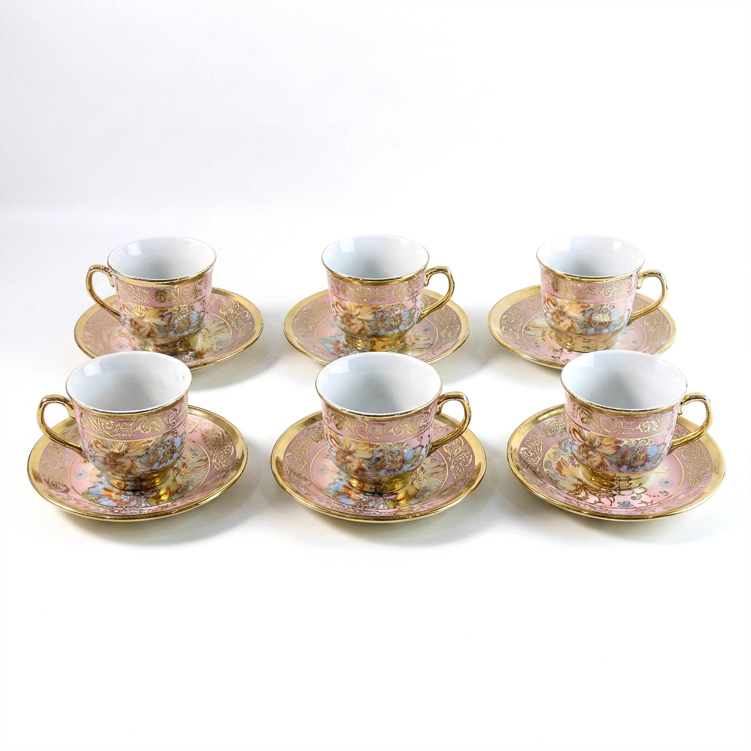 Six pink and gold floral porcelain teacups and saucers with gold rims and handles are neatly arranged on a white surface.