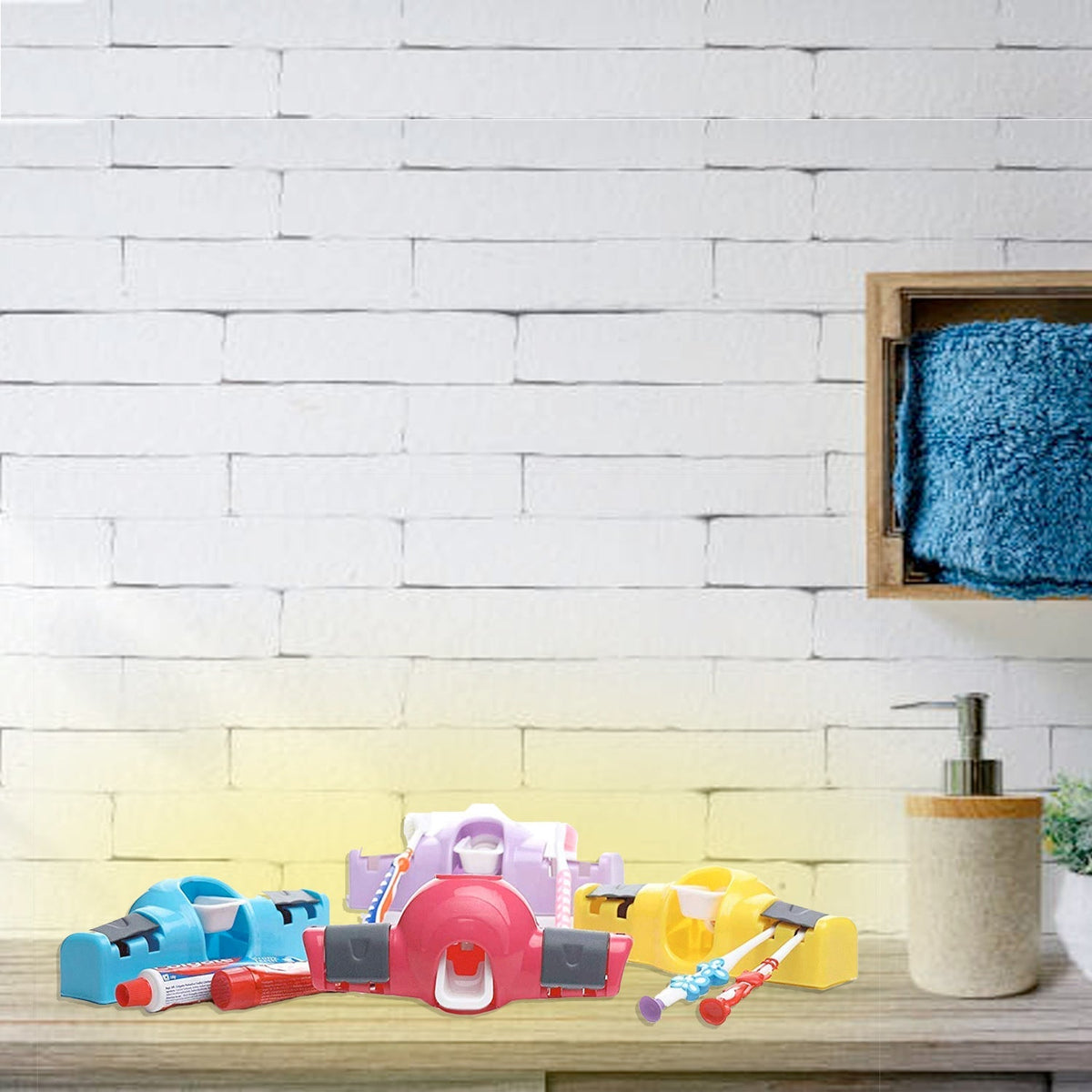 Three toothpaste dispensers in blue, pink, and yellow, with toothbrushes, on a wooden counter against a white brick wall.