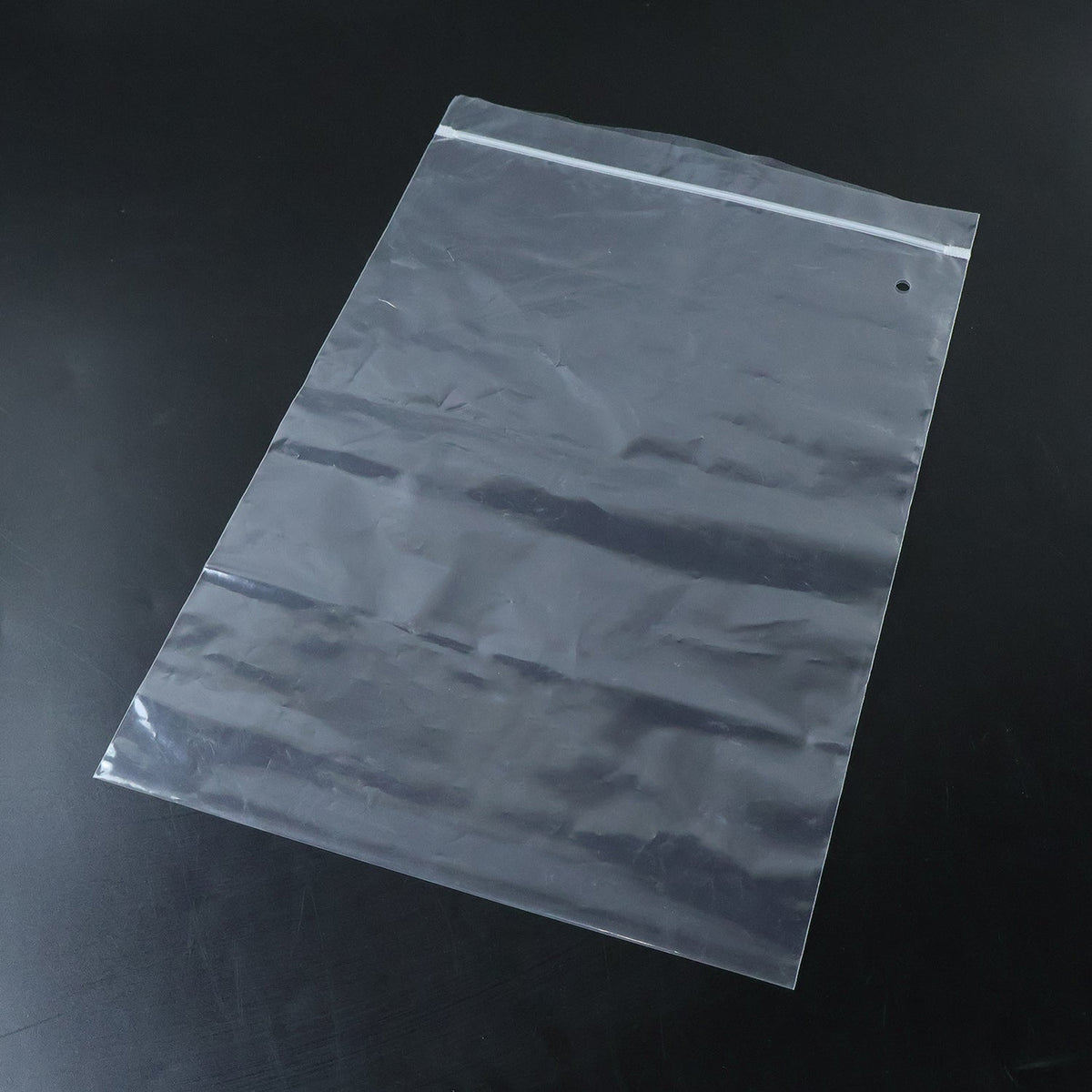 A clear plastic zip lock bag with a hang hole and white zip closure lies flat on a dark black surface.