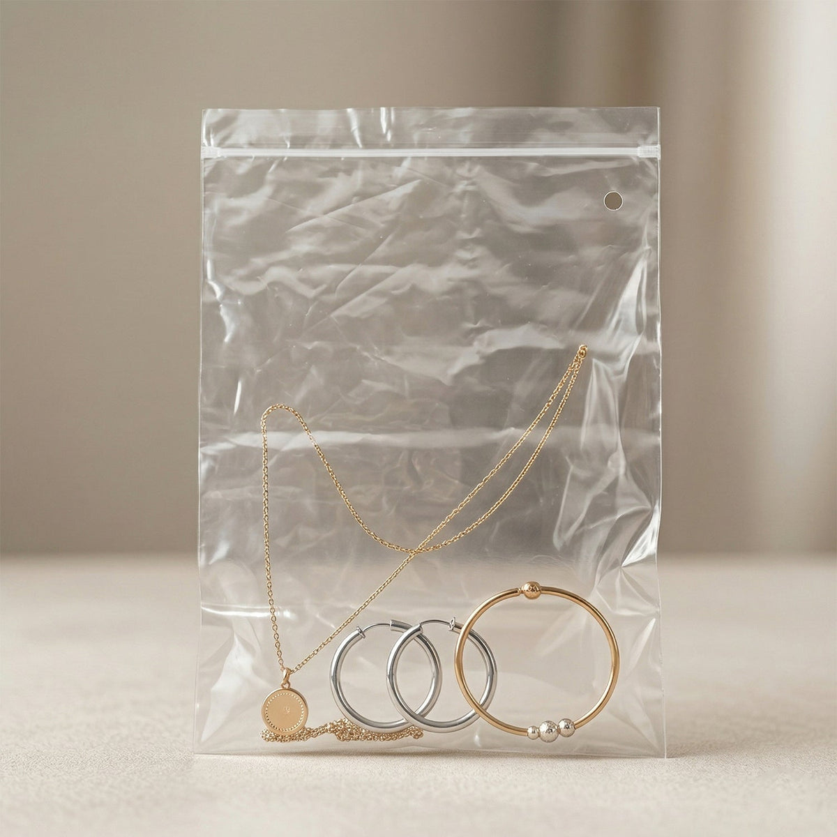 A clear plastic zip lock bag containing a gold necklace, silver hoop earrings, and a gold bracelet.