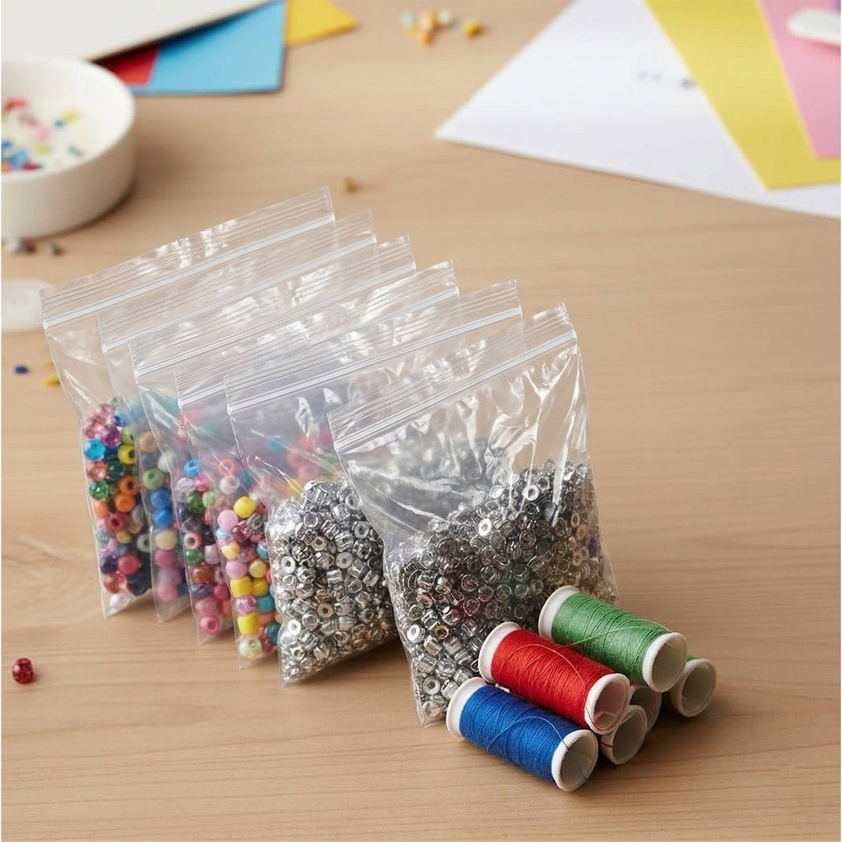 Several clear plastic zip lock bags filled with colorful beads and silver findings, alongside spools of thread.