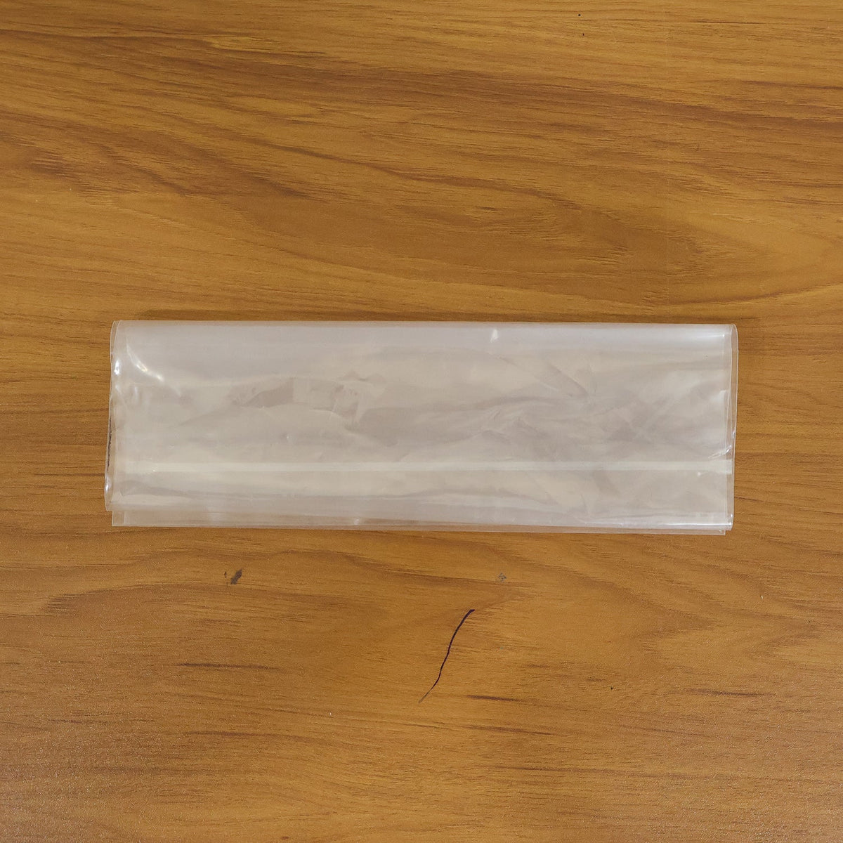 A clear plastic zip lock bag, folded in half lengthwise, rests on a light brown wooden surface.